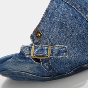 Macro detail of blue denim beret showing orange stitching and brass adjustment buckle