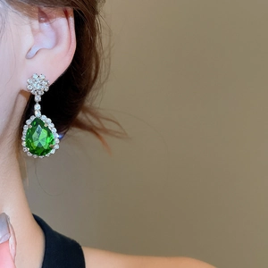 Close-up of elegant emerald water-drop earrings with pavé crystals on a female model