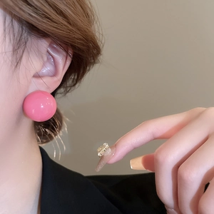 Close-up of bright pink spherical stud earrings in a glossy finish on a female model