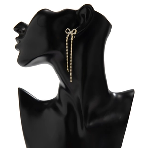 Elegant gold bow earrings with long rhinestone fringe on a black fashion mannequin