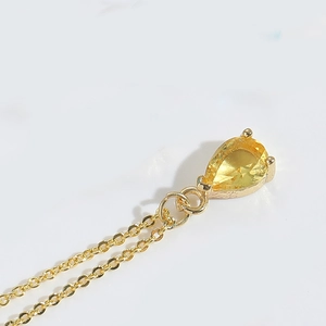 Macro shot of gold teardrop pendant necklace showing detailed prong setting and crystal