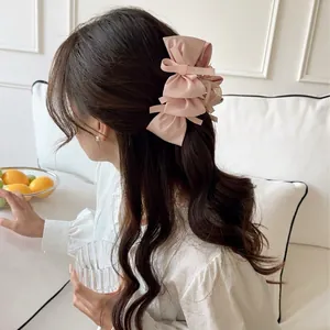 Elegant multi-layered pink ribbon bow hair claw clip worn by model in home setting