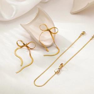 Detail of 18K gold bowknot tassel earrings and snake chain necklace on white fabric