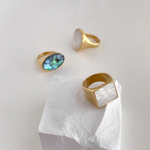 Close-up of geometric natural mother-of-pearl and abalone shell gold rings on stone base