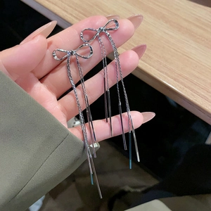 Orecchini lunghi a nappa in argento con design a fiocco minimalista tenuti in mano