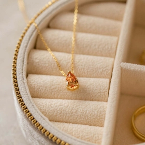 Close-up of a pear-cut orange gemstone pendant on a gold chain in a velvet jewelry box