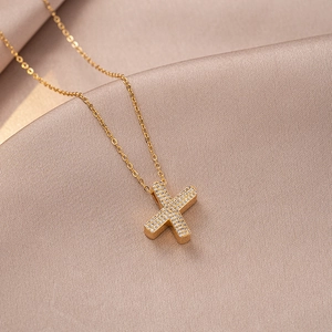 Macro shot of gold letter X pendant with pavé zircons on elegant champagne silk