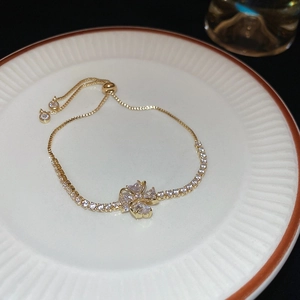 Detail of gold plated hollow clover bracelet with white zircon inlay on white porcelain