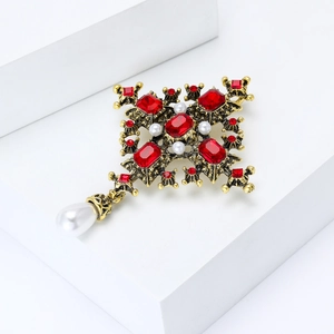Baroque bronze cross brooch with red gems and hanging white pearl on white stand