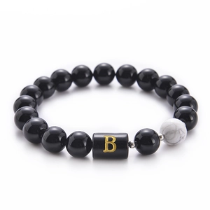 Macro shot of 10mm black onyx and white turquoise beads with golden letter B charm