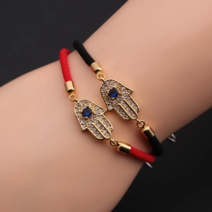 Macro detail of Hamsa Hand charm with blue eye stone on red and black braided bracelets