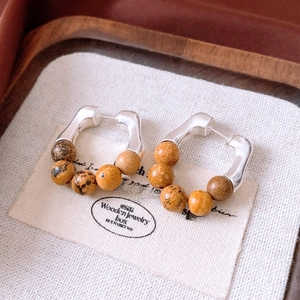 Detail view of silver C-hoop earrings featuring natural brown stone beads on linen