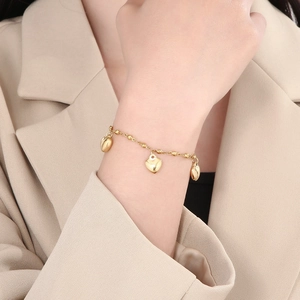 Detail shot of a gold heart charm bracelet worn by a model in elegant office attire