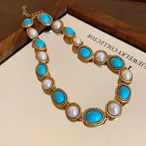 Close-up of vintage gold necklace with blue turquoise and white pearls on mirror