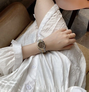Two-tone steel watch with dark dial and date window shown on female wrist with gold ring