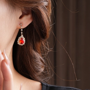 Detail of elegant gold-toned drop earrings with red pear-cut gems and crystal accents