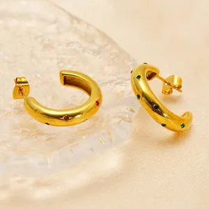 Golden C-shaped earrings with colorful zircon stones on champagne silk and glass