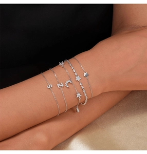 Detail of silver S, N, C and star pendants with zircons on women's delicate chain bracelets