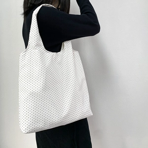 Close-up of a white canvas tote bag with black polka dots worn by a model on shoulder