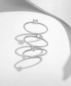 Détail de trois bagues en argent avec pierres carrées, cœur et rondes sur anneau perlé