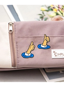 Close-up of cute thumb up enamel pins on a beige pencil case with soft lighting