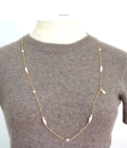 Macro detail of long gold chain necklace with white freshwater pearls on a grey sweater