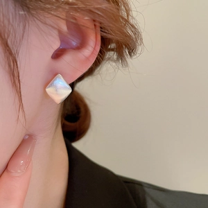 Close-up of geometric diamond-shaped brushed silver earrings on a female model