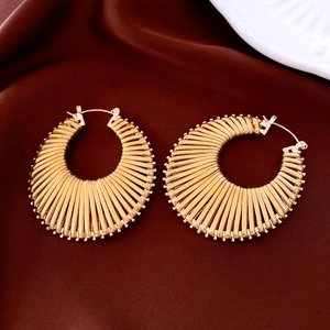 Macro detail of gold round textured hoop earrings with radial patterns on red velvet