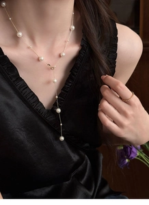 Elegant gold Y-shaped pearl necklace and minimalist ring worn by a model in black silk