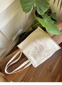 Detail of embroidered 'beloved' lettering on a cream canvas tote bag on wood bench