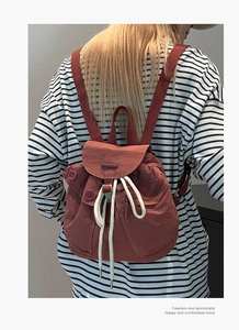 Brick red nylon mini backpack detail showing drawstring closure and side button pockets