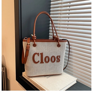Detail of beige canvas tote bag with brown leather trim and Cloos logo under soft light