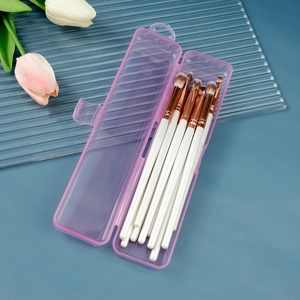 Pink transparent makeup brush storage box with brushes and decorative tulips on a blue desk
