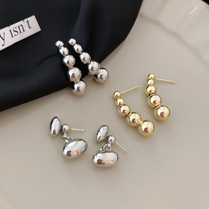 Detail of silver and gold beaded drop earrings and oval studs on a beige tray