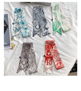 Flat lay of five patterned silk twilly scarves with letters N to R on a white fabric