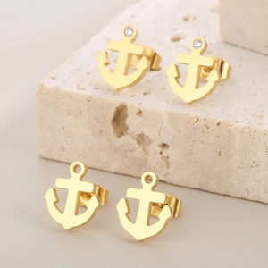 Detailed close-up of gold anchor earrings with embedded white zircons and polished finish