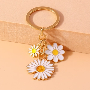 Close-up of golden metal keychain with white and yellow enamel daisy flower charms