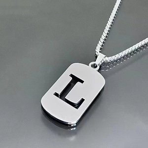 Macro shot of silver stainless steel dog tag pendant featuring a hollow letter L detail