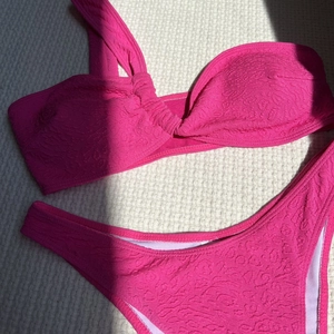 Detail of hot pink bikini showing the unique embossed textured fabric and one-shoulder knot
