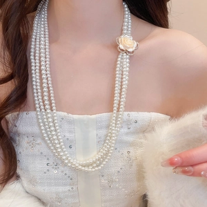 Detail view of multilayer pearl necklace with rhinestone flower clasp worn by a model