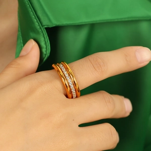 Three-layer gold ring with clear gemstones worn on finger against green satin background