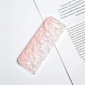 Detailed view of pink acetate wide-tooth comb with marble texture on paper backdrop