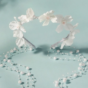 Detail of white flower headband with long pearl tassels on light blue background