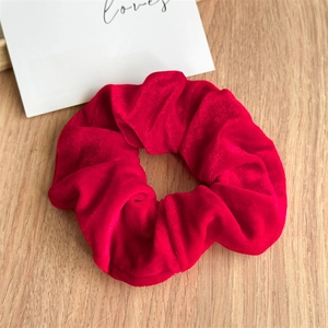Detailed texture of thick red velvet scrunchie showing glossy fiber on wooden background