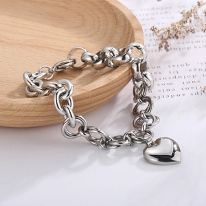 Macro shot of silver-toned chunky link bracelet with a polished heart pendant on a wooden tray