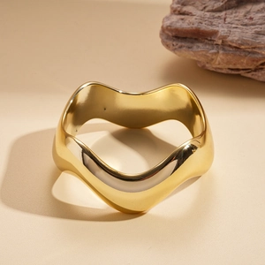 Detail shot of wavy gold geometric bangle on warm beige background with a natural rock accent