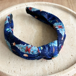 Close-up of navy blue knotted headband with Christmas tree and red bow patterns