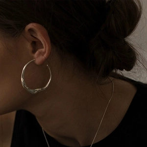 Macro detail of oversized silver irregular lava texture hoop earrings on a model