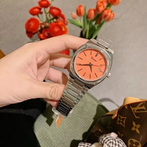 Macro view of silver steel watch featuring a vibrant orange square dial with calendar