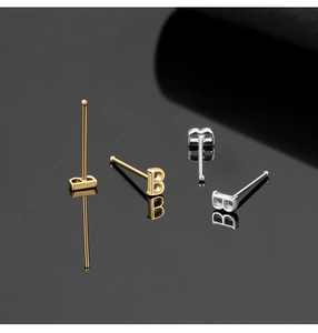 Detail of silver and gold letter B shaped nose studs on reflective black surface
